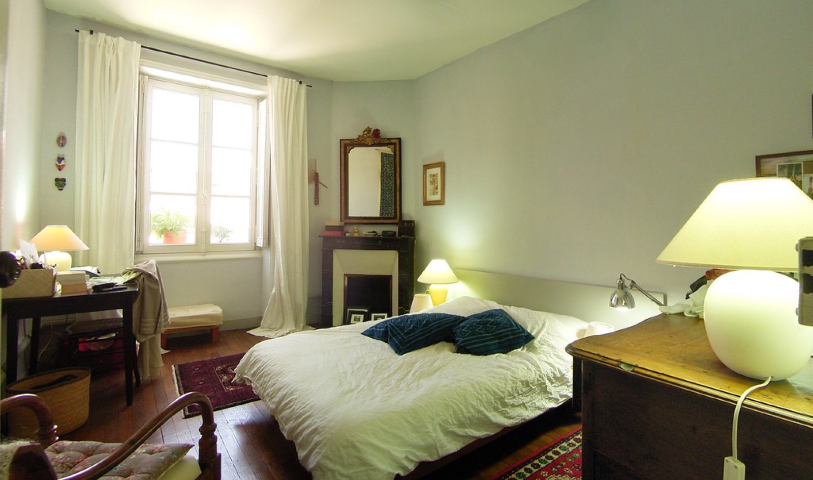 A freshly made bed in a bright guesthouse bedroom with morning light through the window