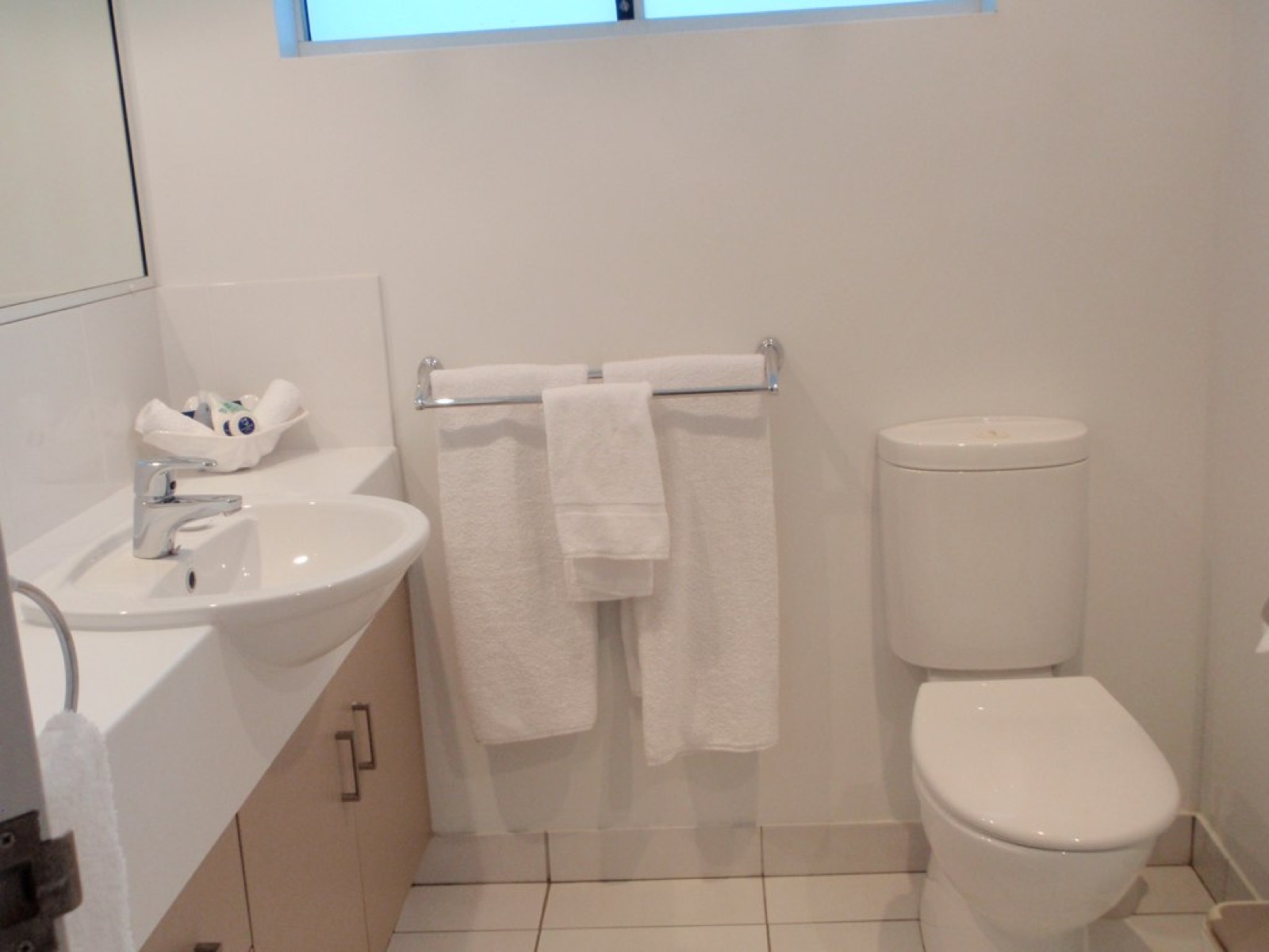 A clean white bathroom with folded towels on the rail and a basin under the mirror