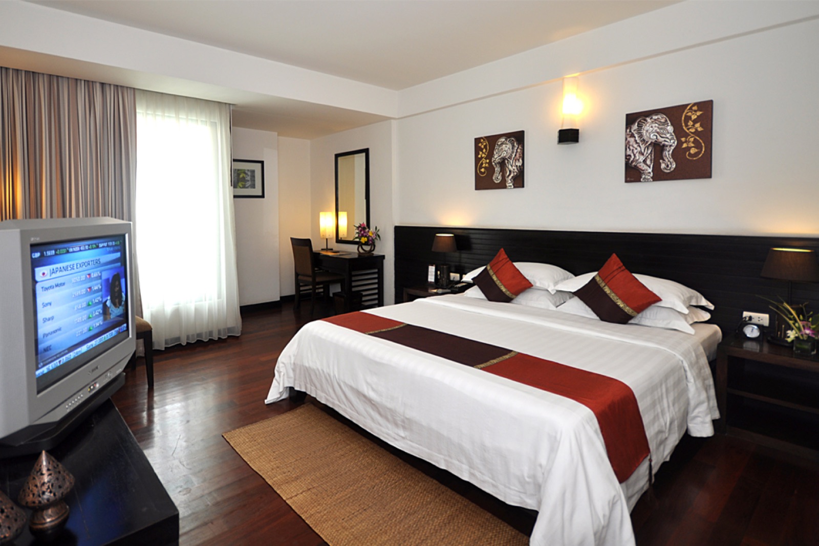 A freshly made hotel bed with white linen and a red runner, ready for the next guest